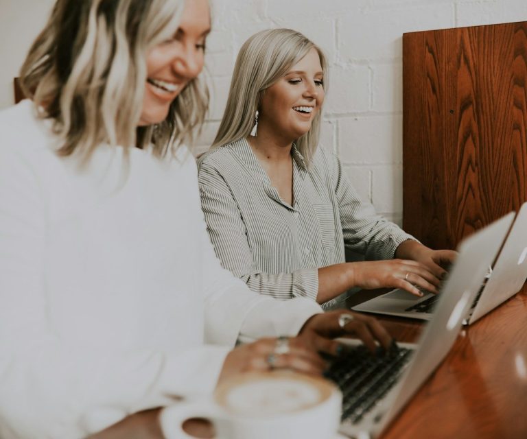 Zwei Frauen sitzen an einem Tisch und arbeiten gemeinsam an einem Laptop.