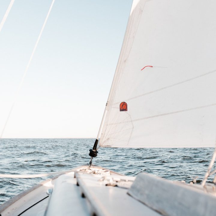 Segelboot mit weißem Segel auf ruhiger See unter blauem Himmel.