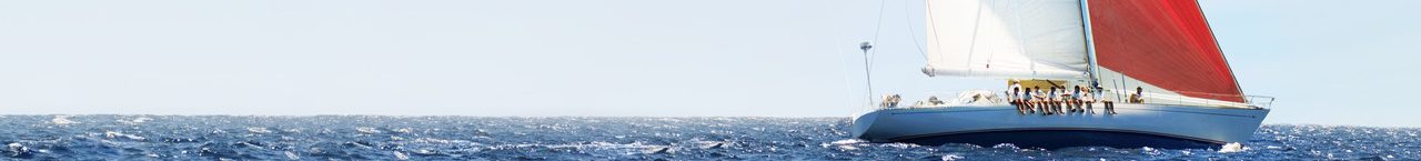 Ein Segelboot mit roten Segeln auf ruhiger See. Mehrere Personen sitzen zusammen an der Reeling und lassen die Beine Baumeln